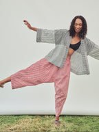A woman posing outdoors in a black and white chevron patterned open-front jacket, red and white striped harem pants, and a black bikini top, set against a plain white studio backdrop with a strip of grass at the bottom.