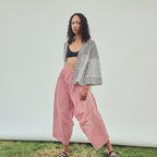 A model stands outdoors against a white backdrop wearing a black and white chevron-patterned open-front jacket, red and white striped harem  pants, a black bandeau top, and slide sandals.