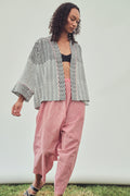 A woman modeling a black and white chevron patterned open-front jacket and red striped pants against a plain light grey backdrop.