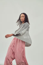 A model wearing a black and white chevron-patterned long-sleeve top and red-and-white striped harem pants, posed against a solid light grey studio background.