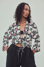 A woman wearing a kimono style jacket tied at the front with a black and burgundy abstract pattern. Tied at the waist over a black bandeau top and black drawstring pants, against a light gray studio background.