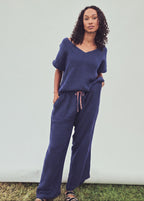 A woman modeling a matching navy blue lounge set consisting of a short-sleeve V-neck top and wide-leg pants with a drawstring waist, standing against a light gray studio backdrop.