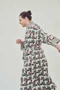 A model wearing a long-sleeved robe with a black and red abstract pattern on off-white background, photographed against a solid light grey studio backdrop.
