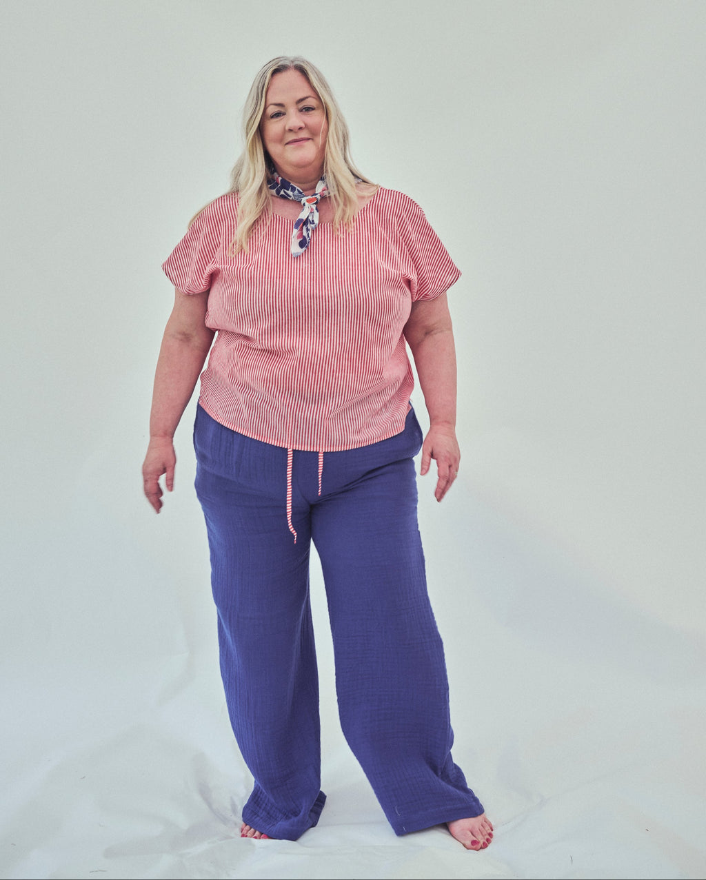 A woman modeling a red striped short-sleeve top and indigo wide-leg pants against a plain light grey studio background.
