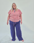 A woman modeling a red striped short-sleeve top and indigo wide-leg pants against a plain light grey studio background.
