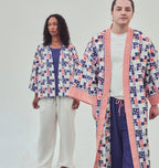 Two models wearing co-ordinating patterned kimono-style jackets and wide-leg pants, standing in front of a white backdrop on grass.