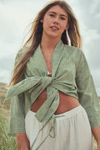 A woman outdoors wearing a light sage green and white striped wrap jacket tied at the waist, paired with white drawstring pants.