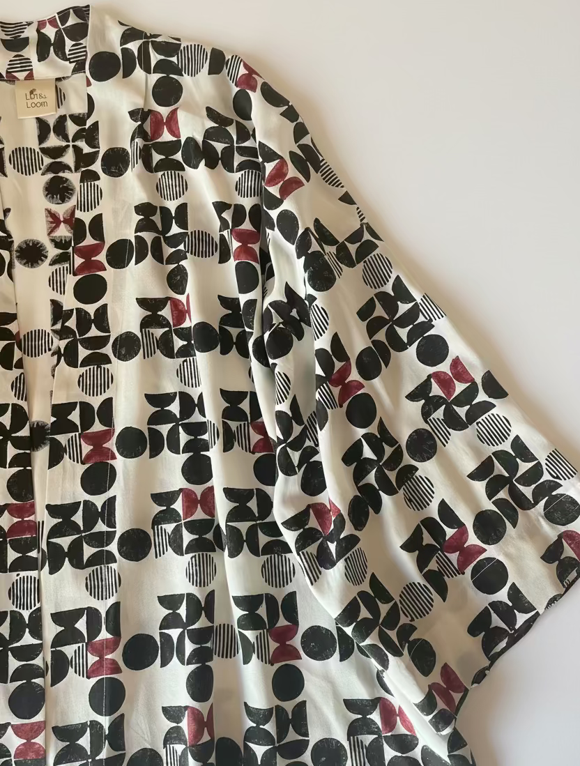A 3/4 sleeve kimono-style jacket with a bold geometric print in black, white and  burgundy laid flat on a white  surface.