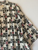 A 3/4 sleeve kimono-style jacket with a bold geometric print in black, white and  burgundy laid flat on a white  surface.