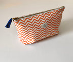 A zippered washbag with an orange and white chevron pattern, featuring a small blue tassel zipper pull and a white brand label that reads 'Loris & Loom'.
