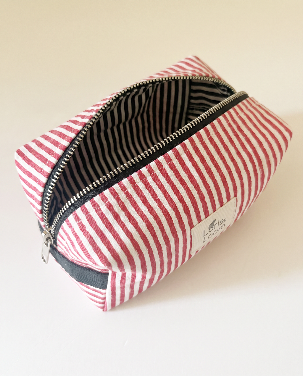 A red and white striped zippered cosmetic pouch with a black handle and a white brand label reading 'Loris & Loom'.